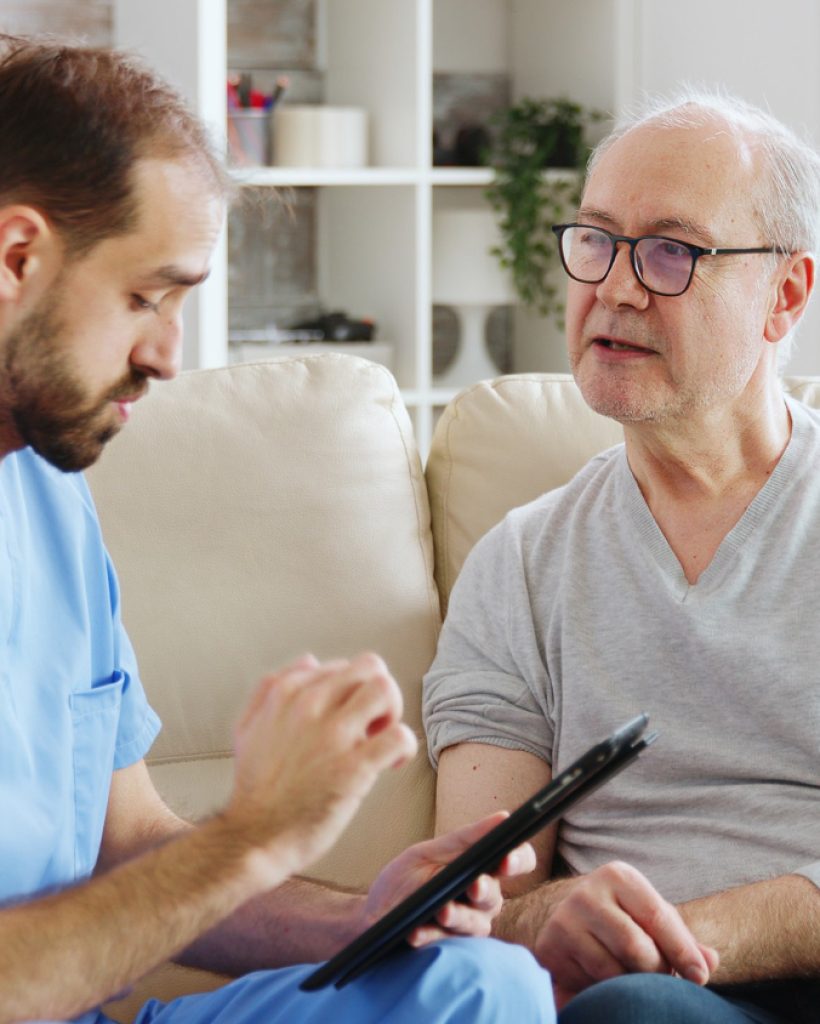 caucasian-male-nurse-talking-with-nursing-home-patient-about-his-health-nurse-is-making-notes-digital-tablet
